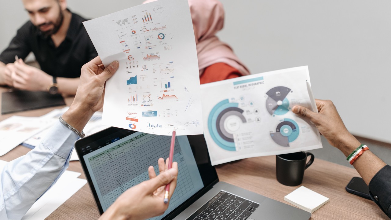 Hands hold printed charts above a laptop during a group discussion.
